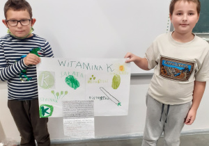 Na zdjęciu dwaj chłopcy z klasy 2 b prezentujący wykonany przez siebie plakat dotyczący witaminy K.